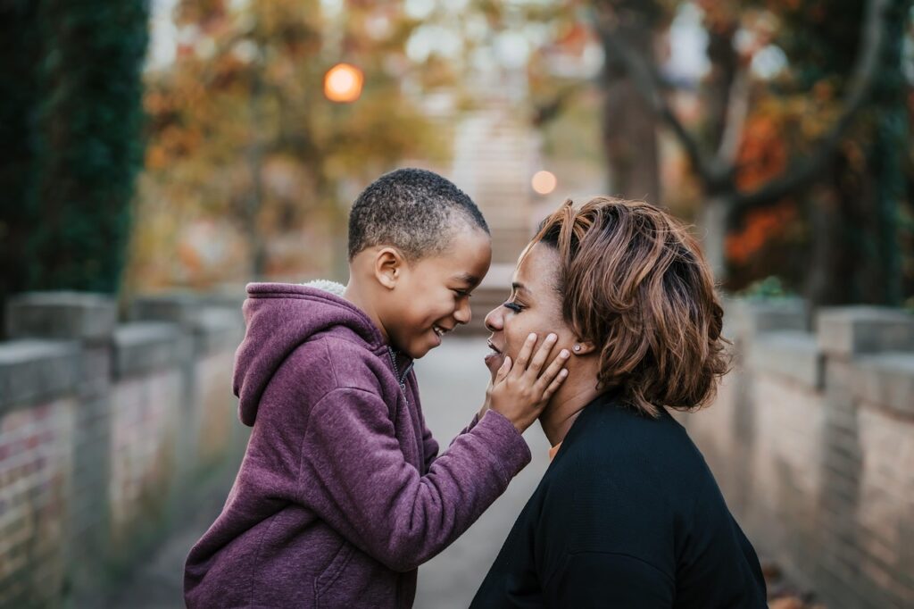 Young son holding his moms cheeks and looking and smiling at his mom who is kneeling or sitting, since her son is taller.